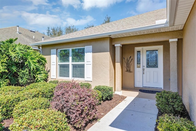 entrance to property featuring a shingled roof and stucco siding