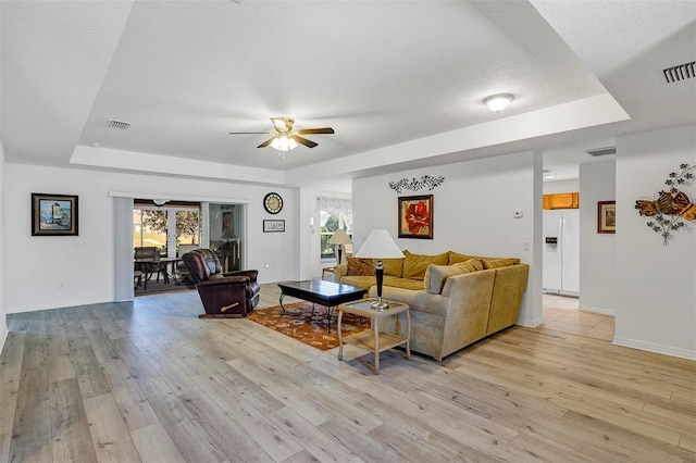 living room featuring light wood finished floors, visible vents, and a tray ceiling