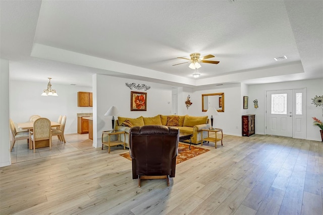 living room featuring light wood-type flooring, a raised ceiling, and a textured ceiling