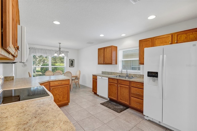 kitchen with light countertops, brown cabinetry, a healthy amount of sunlight, a sink, and white appliances