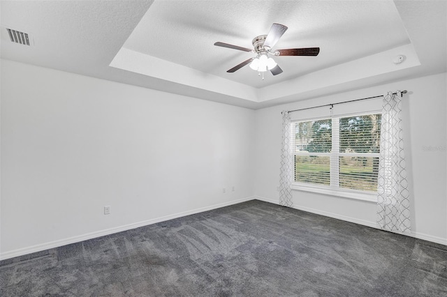 unfurnished room with a textured ceiling, a tray ceiling, visible vents, and baseboards