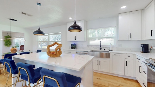 kitchen with visible vents, a kitchen island, a kitchen breakfast bar, light stone countertops, and a sink