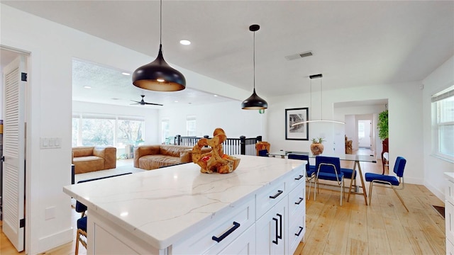 1930 Hilltop Dr, Mount Dora, FL 32757 - kitchen featuring light stone counters, a kitchen island, visible vents, white cabinets, and light wood-style floors