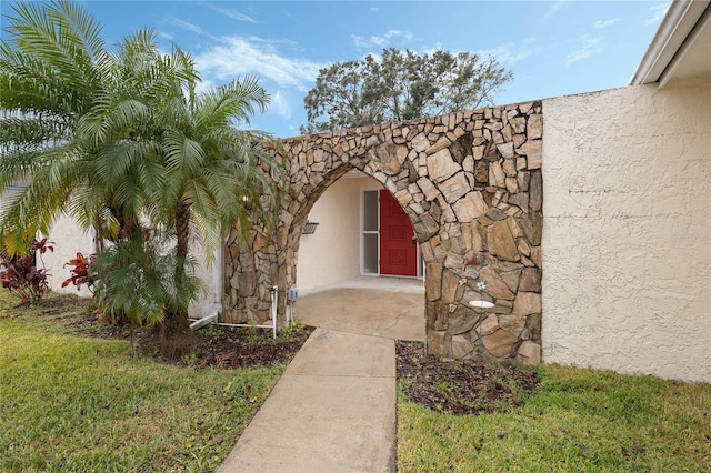 view of exterior entry with a yard and stucco siding