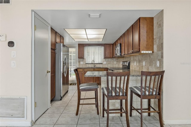 kitchen featuring tasteful backsplash, dark countertops, visible vents, appliances with stainless steel finishes, and brown cabinetry