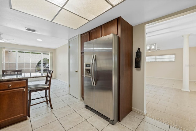 kitchen with light tile patterned floors, stainless steel fridge, decorative columns, and dark stone counters