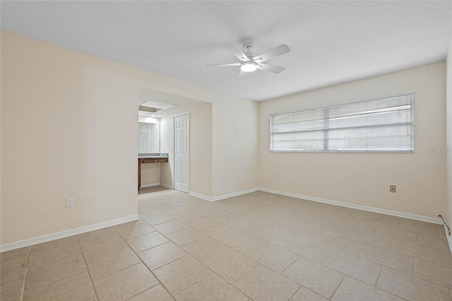 empty room with light tile patterned floors, ceiling fan, baseboards, and a textured ceiling