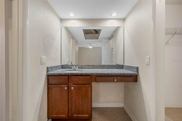 bathroom featuring a walk in closet, a textured wall, vanity, and tile patterned floors