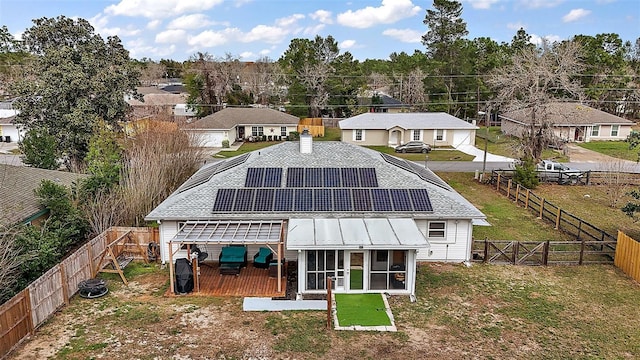 rear view of house with a sunroom, a fenced backyard, and roof mounted solar panels