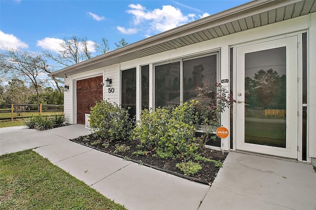 entrance to property featuring an attached garage and fence