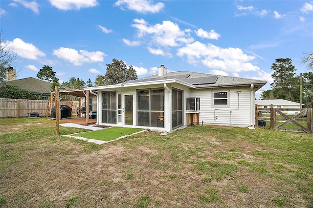 rear view of house with a fenced backyard, solar panels, a sunroom, a yard, and a chimney