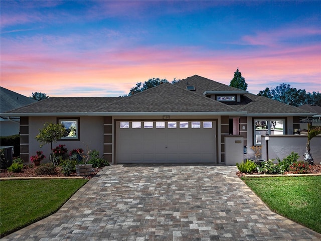 view of front facade featuring a garage, decorative driveway, roof with shingles, and stucco siding