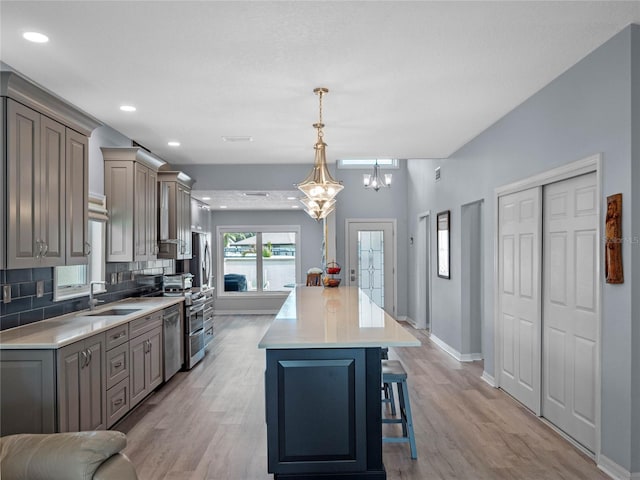 kitchen with a breakfast bar area, a sink, light countertops, gray cabinets, and decorative backsplash