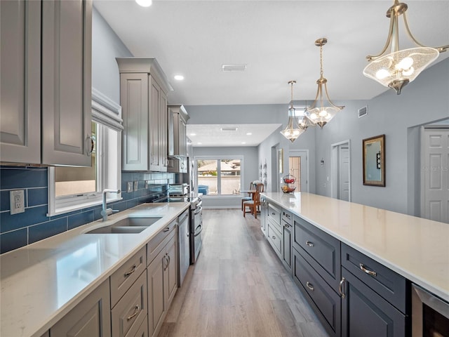 kitchen with light wood finished floors, visible vents, decorative backsplash, a sink, and beverage cooler