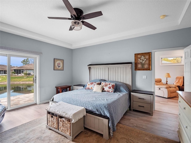 bedroom with light wood-style floors, access to outside, a raised ceiling, and ceiling fan