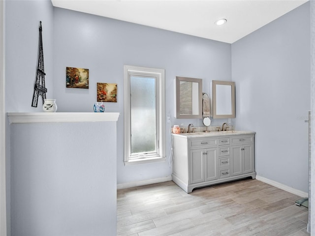 full bathroom with double vanity, baseboards, a sink, and wood finished floors