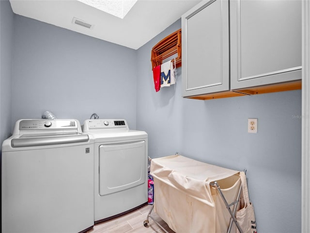 laundry area with a skylight, washing machine and clothes dryer, cabinet space, visible vents, and wood tiled floor