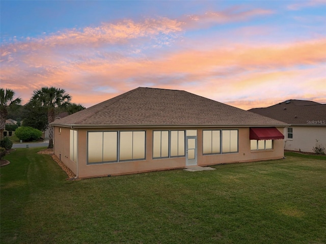 rear view of property with roof with shingles, a yard, and stucco siding