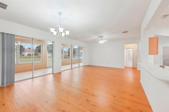 unfurnished living room with light wood-type flooring, visible vents, and ceiling fan with notable chandelier