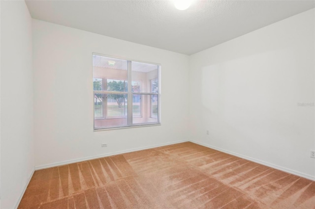 empty room featuring light carpet, baseboards, and a textured ceiling