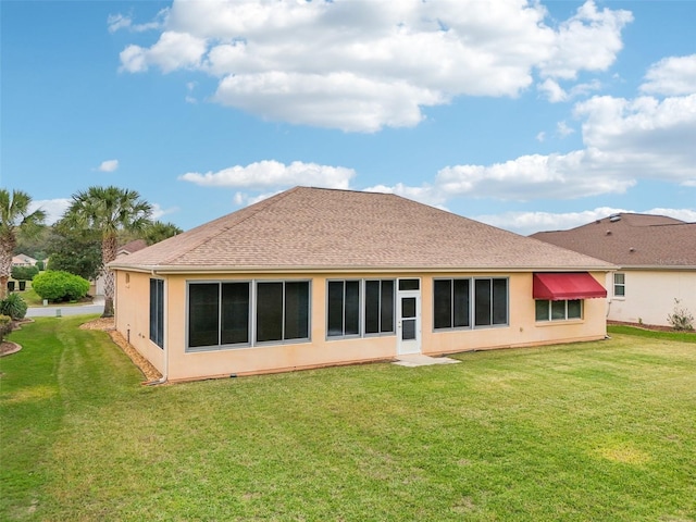 rear view of house with roof with shingles, a lawn, and stucco siding