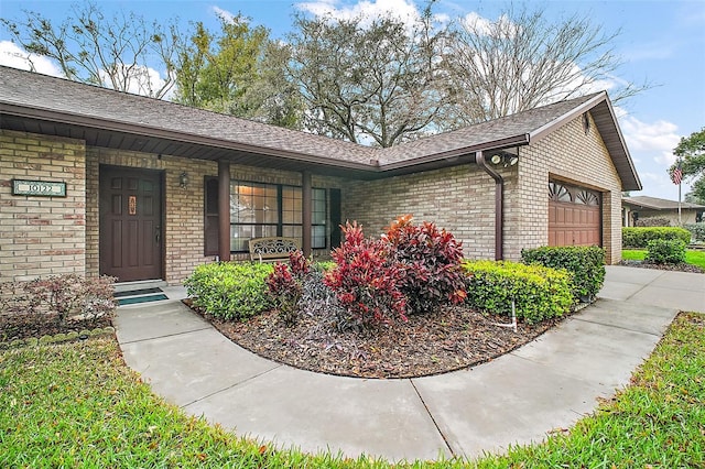 entrance to property with a garage, covered porch, brick siding, concrete driveway, and roof with shingles