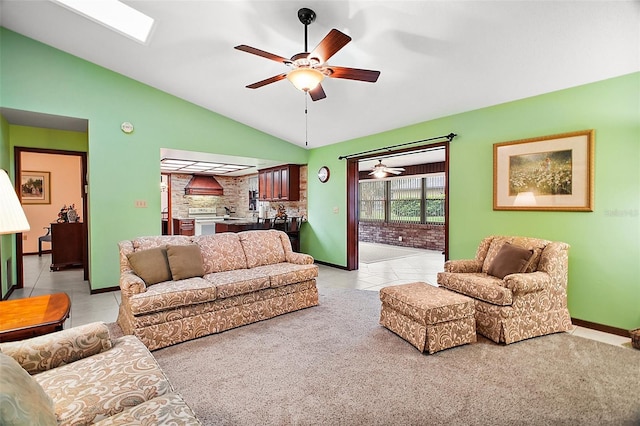 living area featuring a ceiling fan, baseboards, lofted ceiling with skylight, and light tile patterned floors