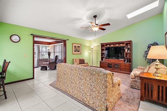 tiled living room with vaulted ceiling with skylight, baseboards, and ceiling fan