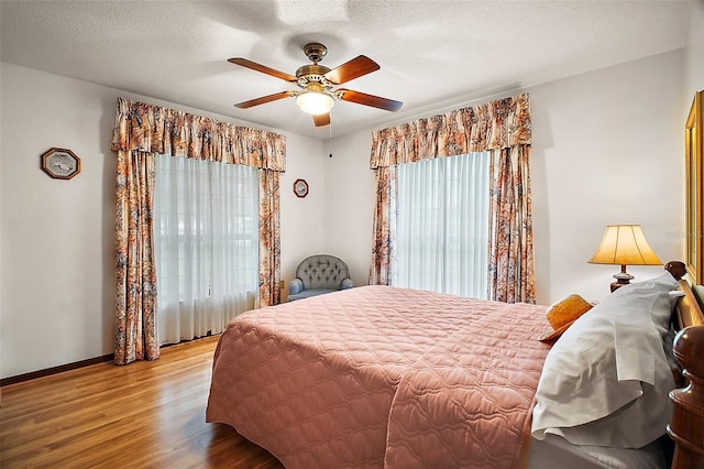 bedroom with a ceiling fan, a textured ceiling, baseboards, and wood finished floors