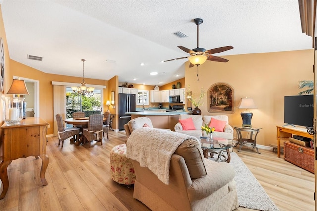 living room featuring lofted ceiling, visible vents, light wood-style flooring, and ceiling fan with notable chandelier