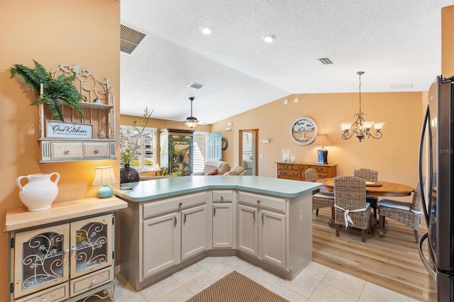 kitchen featuring a peninsula, visible vents, vaulted ceiling, and freestanding refrigerator