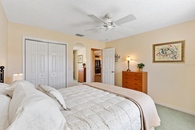 carpeted bedroom with arched walkways, ceiling fan, a textured ceiling, visible vents, and a closet