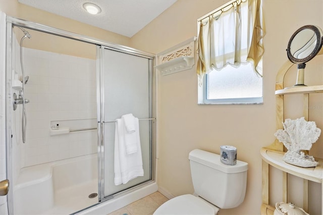 bathroom featuring toilet, a shower stall, a textured ceiling, and tile patterned floors