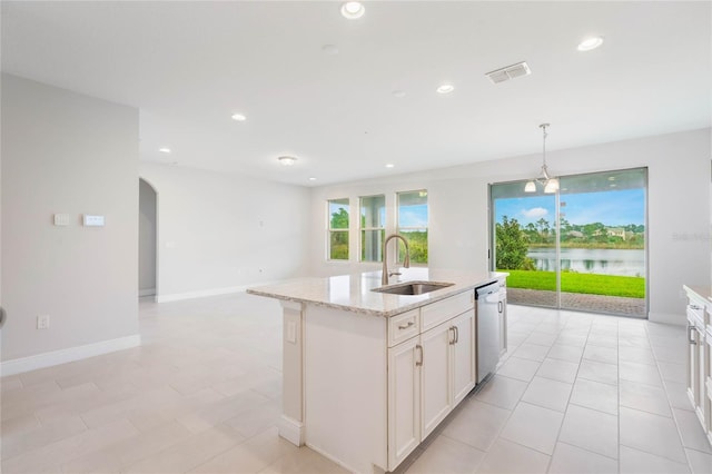 kitchen with a center island with sink, arched walkways, a water view, stainless steel dishwasher, and a sink