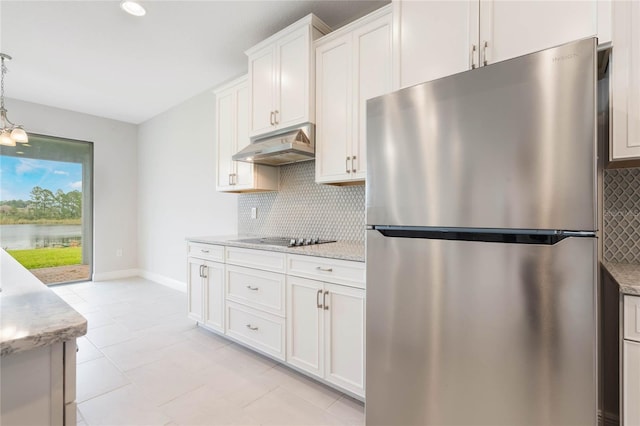 kitchen with tasteful backsplash, freestanding refrigerator, black electric stovetop, under cabinet range hood, and white cabinetry