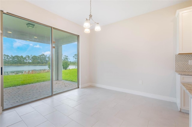 unfurnished dining area featuring a water view, a notable chandelier, and baseboards