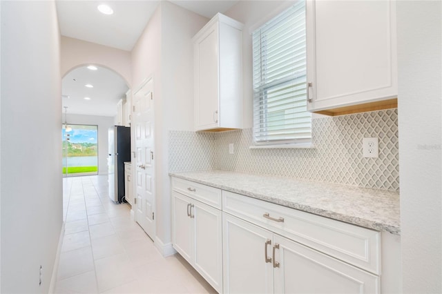 kitchen with arched walkways, tasteful backsplash, freestanding refrigerator, white cabinets, and light tile patterned flooring