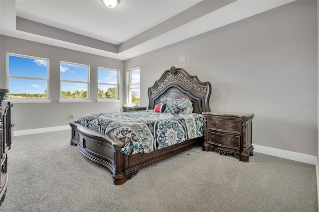 carpeted bedroom featuring baseboards and a tray ceiling