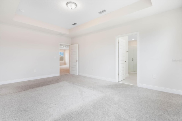 unfurnished bedroom featuring light carpet, visible vents, a tray ceiling, and baseboards