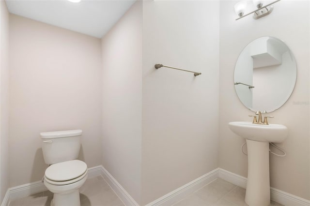 bathroom with toilet, tile patterned flooring, baseboards, and a sink