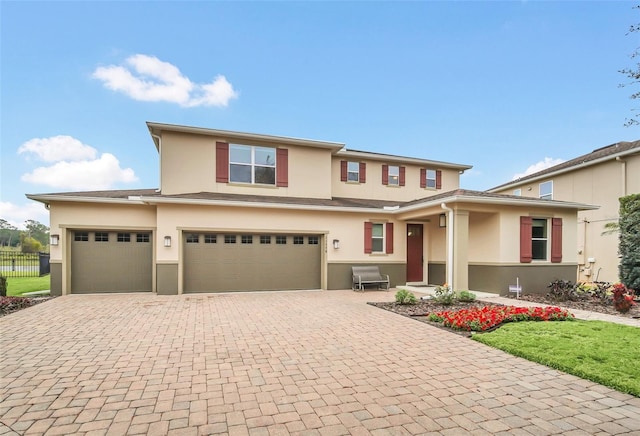 view of front facade featuring a garage, fence, decorative driveway, and stucco siding