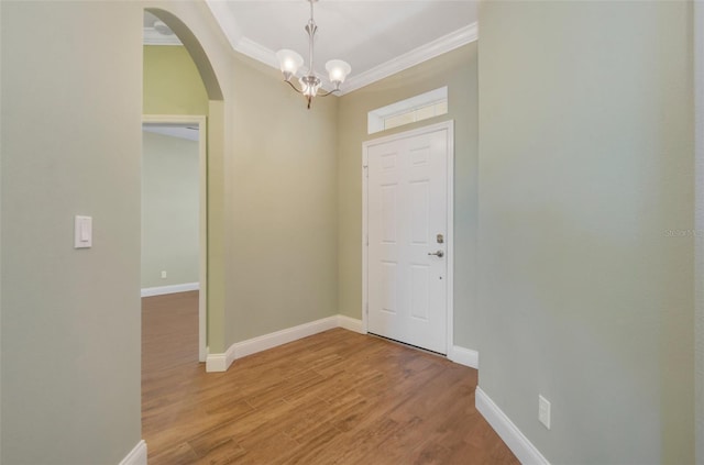 entryway featuring arched walkways, crown molding, light wood-style flooring, and baseboards