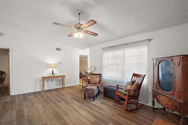 living area featuring a textured ceiling, wood finished floors, visible vents, a ceiling fan, and vaulted ceiling