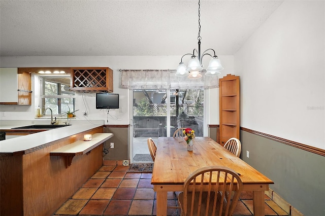 dining room with a wainscoted wall, dark tile patterned flooring, a textured ceiling, and a notable chandelier