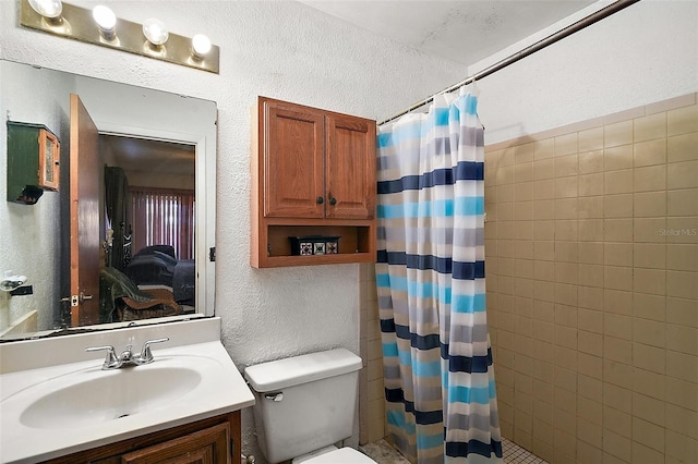 full bath featuring toilet, a textured wall, a tile shower, and vanity