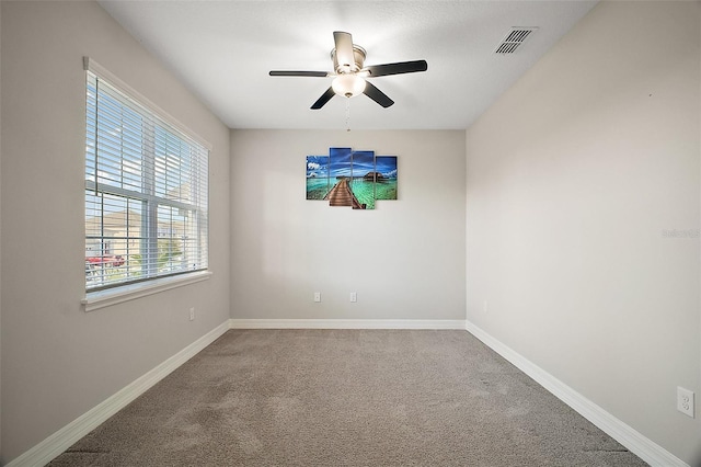 carpeted spare room with baseboards, visible vents, and a ceiling fan