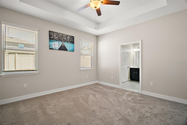 spare room featuring a tray ceiling, light colored carpet, ceiling fan, and baseboards