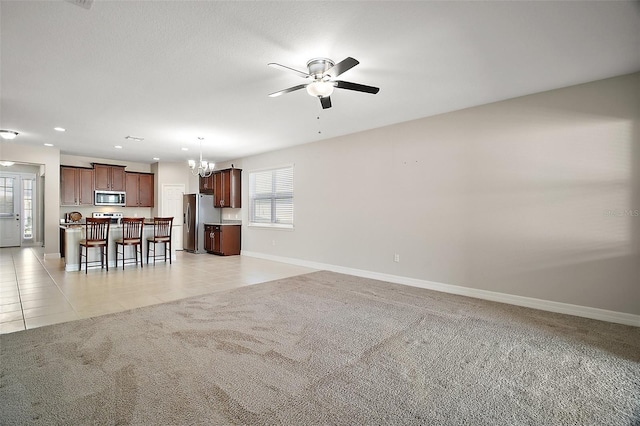 unfurnished living room featuring light carpet, light tile patterned floors, ceiling fan with notable chandelier, and baseboards