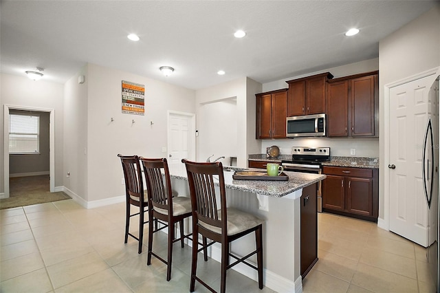 kitchen featuring appliances with stainless steel finishes, stone countertops, a center island with sink, and a breakfast bar area