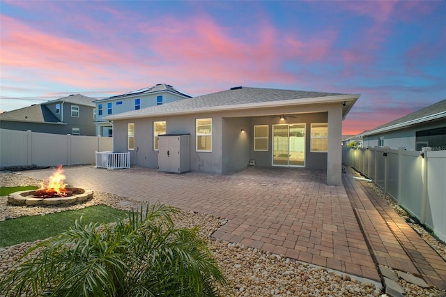 back of property at dusk with a fire pit, central AC, a fenced backyard, and stucco siding